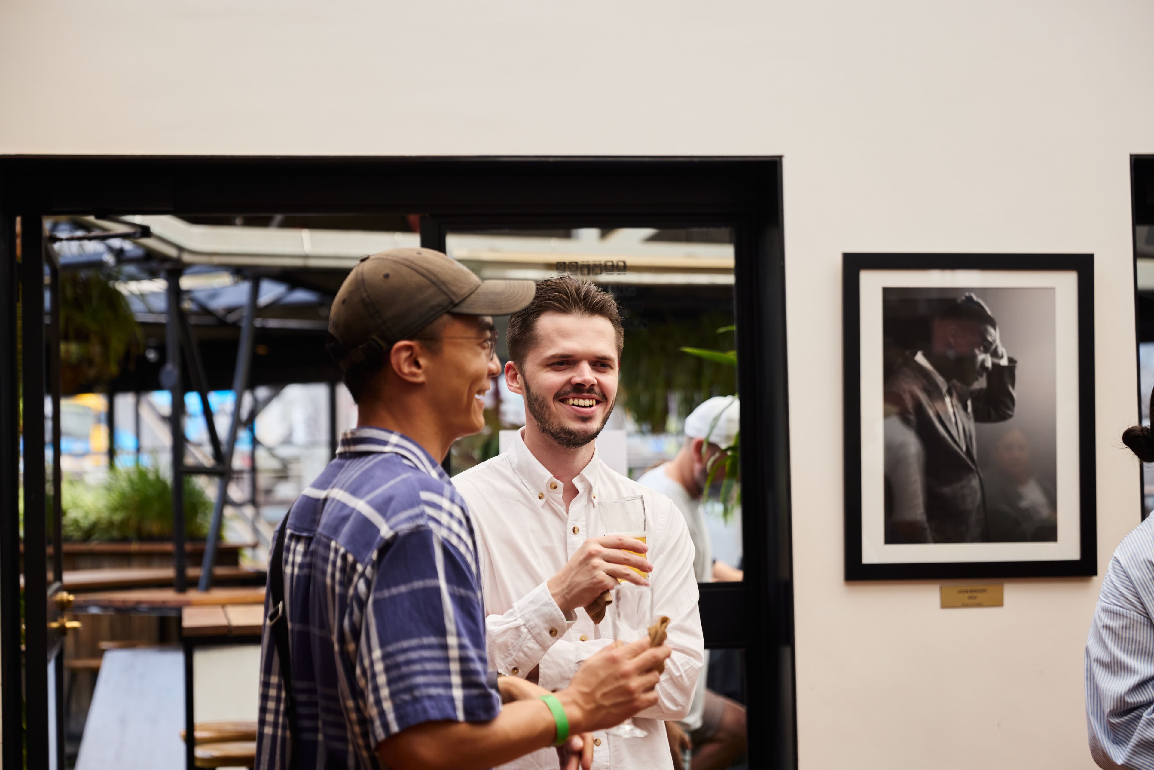 Two people chat indoors near a doorway at Compose event, holding food and drinks.