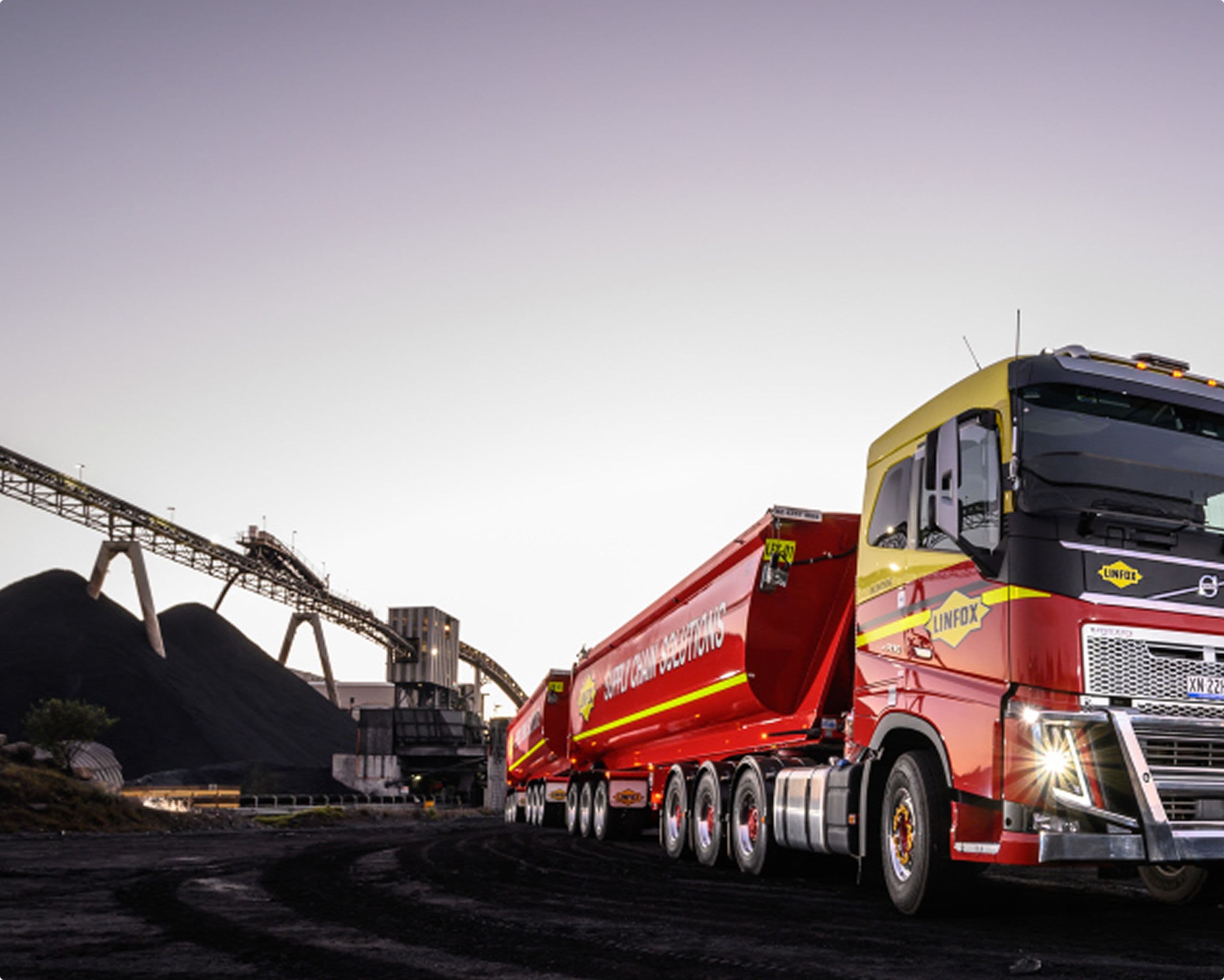 A large, modern Linfox truck and trailer—painted in Linfox’s signature yellow and red—are parked at an industrial site during twilight. The truck is positioned on black gravel near large piles of material and conveyor structures, evoking a busy and capable logistics operation. alt text: alt text: Image 1: A digital dashboard from Linfox’s Track & Trace system displays a list of shipment records. The screen features columns for shipment ID, reference number, pickup and delivery locations, along with the delivery status such as “Delivered,” “In Transit,” “Processed,” or “Last Mile.” Filters for date, location, and status appear at the top, and the logged-in user is “Elyse Denny.” Image 2: A mobile-friendly Linfox tracking interface on a yellow background shows a shipment’s progress timeline. Steps include “Created,” “Processed,” “In Transit” (with estimated time of arrival), and “Delivered.” The delivery location (First Choice Liquor, Glen Iris, VIC) and delivery time window are listed at the bottom. Image 3: A row of large, modern Linfox trucks is parked outdoors. The trucks are painted in the signature Linfox colours of yellow and red, with bold Linfox logos visible above the windscreen and on the side. The trucks are Scania brand, with the model “P450” displayed. The sky is partly cloudy, and the trucks are lined up on a concrete surface.